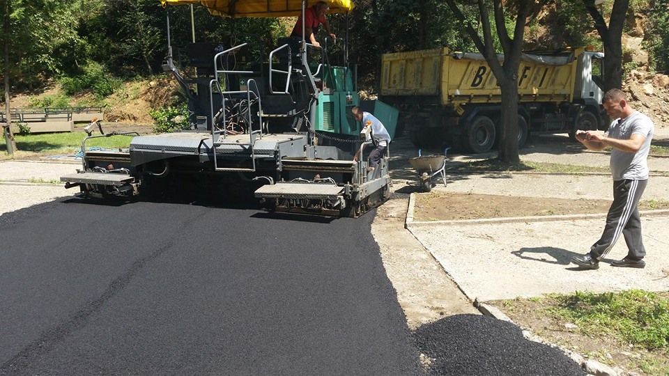 Finišer ugrađuje asfalt dok radnik prati nivelaciju